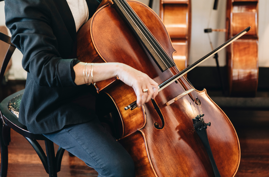 Person playing a cello in a room with other cellos in the background